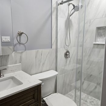 Simple Roofing - Bathroom #2 Shower - A compact bathroom features a walk-in shower with glass doors, a toilet, and a vanity with a marble countertop and dark wood cabinet. - Roofing Near Me - Wayne, New Jersey