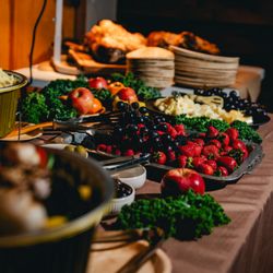 Castle Town Catering - A vibrant spread of fruits and cheese on a tan tablecloth, with roasted meat in the background.