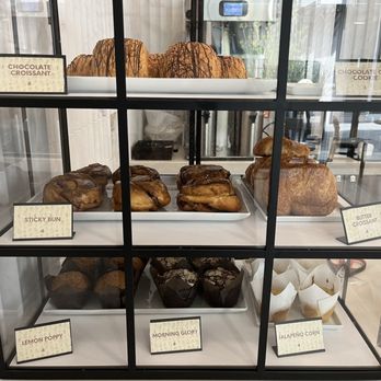 Perks - A glass display case showcases baked items such as croissants, muffins, and cookies, each labeled with small signs indicating their names. - Coffee & Tea Near Me - Phoenix, Arizona