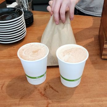 Analog Coffee - a person holding a bag and two cups of coffee - Cafes Near Me - Seattle, Washington