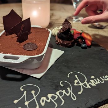 TOCA - Chocolate mousse served in a white dish, decorated with chocolate shards, on a black slate plate with 'Happy Anniversary' written in white chocolate. - Italian Near Me - Toronto, Ontario