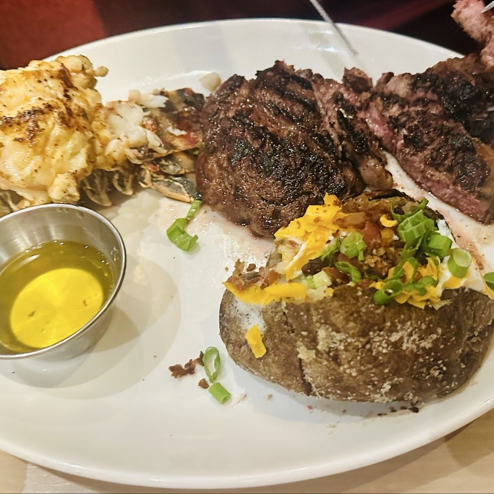 Firebirds Wood Fired Grill - 12oz Aged Ribeye served with a Loaded Baked Potato & Lobster Tail - Steakhouses Near Me - Omaha, Nebraska Firebirds Wood Fired Grill - 12oz Aged Ribeye served with a Loaded Baked Potato & Lobster Tail - Steakhouses Near Me - Omaha, Nebraska