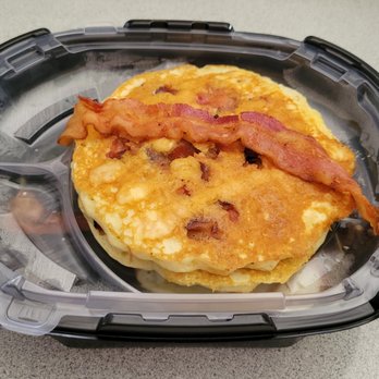 IHOP - The top section has 2 pancakes with bacon pieces inside and a strip of candied bacon. - A breakfast sandwich featuring a folded egg and crispy bacon strip on top, contained within a clear plastic food storage container. The container is placed on a gray, textured surface, likely a countertop or table. - Breakfast & Brunch Near Me - Clinton, Maryland