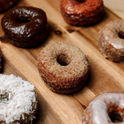 Bismarck Doughnuts - This image displays a tempting variety of Bismarck's gluten-free doughnuts on a wooden board, featuring chocolate-glazed, pow...