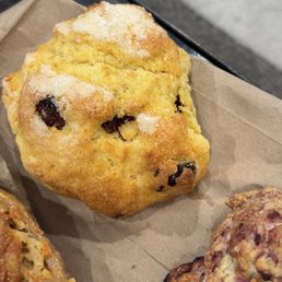 A golden-brown muffin with chocolate chips on a brown paper liner, likely from a bakery or cafe.
