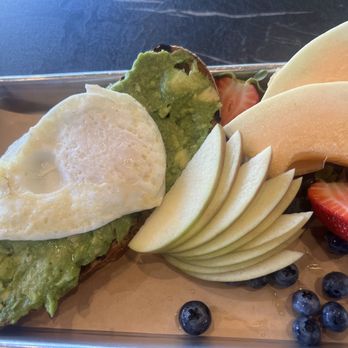 Provisions South - Avocado Toast - A breakfast plate featuring avocado toast with a fried egg, sliced pears, strawberries, blueberries, and other fresh fruit on a metal tray. - Coffee & Tea Near Me - Eugene, Oregon