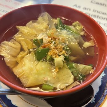 Thai Station - Cabbage soup included with lunch, great! - A bowl of cabbage soup with chopped green onions and fried garlic garnishes, served in a red bowl on a decorative plate. - Thai Near Me - Payson, Arizona