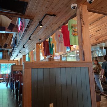Dockside Willies - Interior of a restaurant with wood-paneled ceiling and walls, hanging colorful T-shirts, security cameras, and a partial view of customers and staff. - Seafood Near Me - Wormleysburg, Pennsylvania