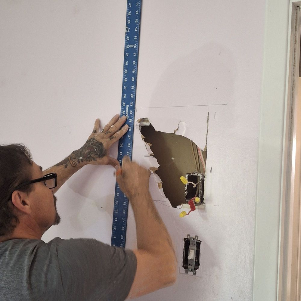 Drywall contractor measuring a wall patch around electrical boxes
