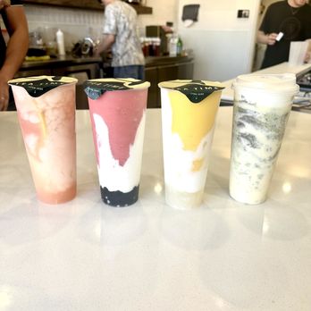 Tea Time - Four drinks with different colors and toppings are placed on a white countertop in a tea shop setting. - Coffee & Tea Near Me - Albuquerque, New Mexico