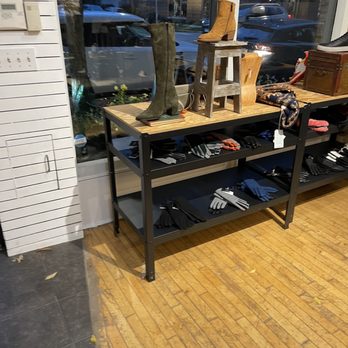 A Pied - A retail store interior features a table with boots, gloves, and accessories, positioned near a large window showing parked cars outside. - Shoe Stores Near Me - Chicago, Illinois