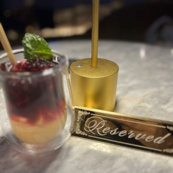 Morse Code Lounge - Bar tender Ian's speciality drink - A layered cocktail garnished with berries and mint in a glass, a gold table number holder, and a reserved sign on a marble table at a lounge or restaurant. - Wine Bars Near Me - Winter Park, Florida