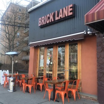 Bricklane Curry House, Upper Montclair, NJ - Exterior view of Brick Lane restaurant with outdoor tables, orange chairs, and a sign on the building. - Indian Near Me - Montclair, New Jersey