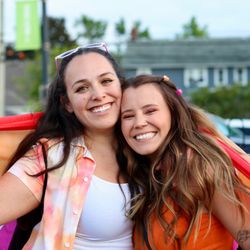 The Larson Lens - Two people standing close to each other, smiling, and holding a lesbian pride flag around themselves.