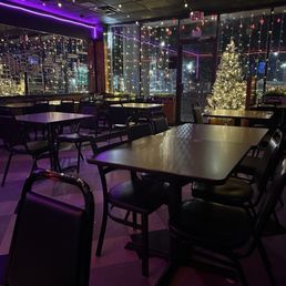 interior - A dimly lit restaurant interior features tables and chairs, with large windows decorated with string lights and a Christmas tree.