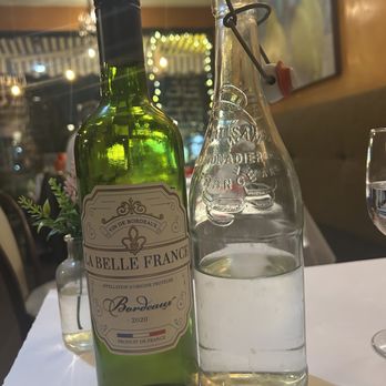 Cafe Monet - BYOB - A green wine bottle labeled 'La Belle France Bordeaux 2020' and a clear glass water bottle are on a white tablecloth in a restaurant setting. - French Near Me - Millburn, New Jersey