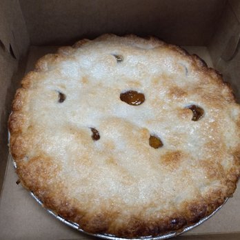 Sergio's Bakery and Cafe - This Friday's dessert was apple or cherry pie. I got apple. - A round cherry pie with a golden, flaky crust and a slightly uneven surface is displayed inside a cardboard box. The crust has a sugary glaze and small holes revealing the cherry filling underneath. The pie appears freshly baked and is placed in a disposable aluminum pie pan, suitable for takeaway or serving. - Bakeries Near Me - Albuquerque, New Mexico