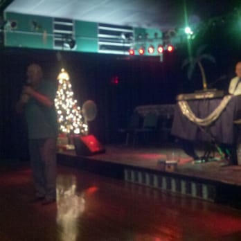 Colorama Music - a man standing on a stage with a christmas tree in the background - Music Venues Near Me - Hudson, Florida Colorama Music - a man standing on a stage with a christmas tree in the background - Music Venues Near Me - Hudson, Florida