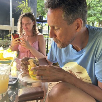 Rico Arepa - Outdoor dining area. Handsome man eating pork arepa. Lovely daughter taking a photo of her arepa! - Venezuelan Near Me - Manatí, Puerto Rico Rico Arepa - Outdoor dining area. Handsome man eating pork arepa. Lovely daughter taking a photo of her arepa! - Venezuelan Near Me - Manatí, Puerto Rico