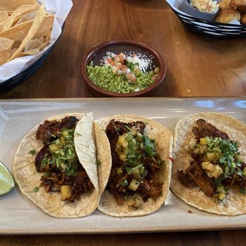 Nada - Pork Al Pastor tacos - Three pork al pastor tacos topped with chopped pineapple and herbs, served on a rectangular plate with a lime wedge. - Mexican Near Me - Cincinnati, Ohio