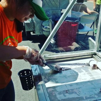 Cha-Yen - a woman in an orange shirt and a green hat cutting meat on a grill - Food Trucks Near Me