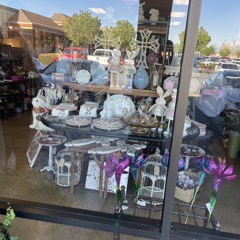Authentique - The window showcases an assortment of decorative home accessories such as vases, figurines, and wind chimes, with reflections of the parking lot and trees outside. - Home Decor Near Me - Fresno, California