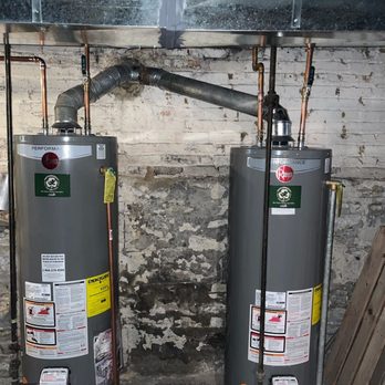Fast Plumbing 247 - 2 Rheem Performance 40 gallon water heaters - Two Rheem Performance 40-gallon water heaters are positioned side by side against a brick wall in a basement or utility area. - Water Heater Installation/Repair Near Me