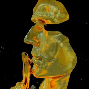 AutoZone - The salesman - A detailed glass sculpture shows a person's face in profile, with features such as the nose, lips, and chin clearly defined. The figure has a finger held up to the lips in a gesture of silence. The sculpture is made of transparent and colored glass, with orange and yellow hues, and is set against a black background, highlighting its intricate craftsmanship. - Auto Parts & Supplies Near Me - Flushing, New York