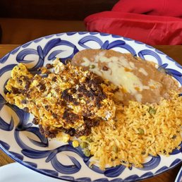 Chorizo - A colorful plate features Mexican rice, refried beans with melted cheese, and a casserole with eggs and meat, served at a restaurant.