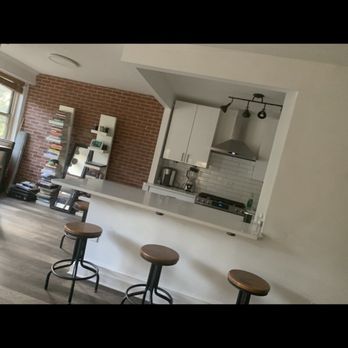Cedeno Contracting - Renovated kitchen - A kitchen featuring a breakfast bar with three wooden stools, white cabinets, and a brick accent wall with bookshelves. - General Contractors Near Me