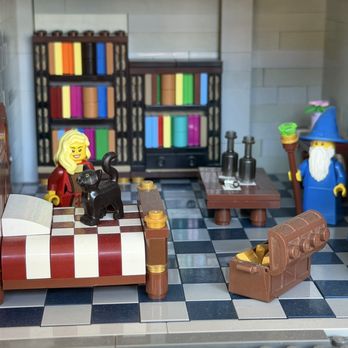 eBricks Outlet - LEGO figures of a wizard, a woman, and a black cat are in a room with bookshelves, a table, and a treasure chest, resembling a fantasy or magical setting. - Toy Stores Near Me - Grand Junction, Colorado