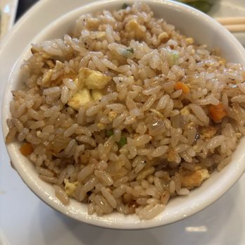 Benihana - HIBACHI FRIED RICE - A bowl of fried rice containing vegetables, scrambled eggs, and soy sauce, served on a white plate. - Sushi Bars Near Me - Concord, California