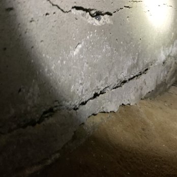 ClayCon Developers - Old foundation - A concrete foundation wall with visible cracks, situated above a dirt floor, illuminated by a light source. - Foundation Repair Near Me