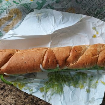 Subway - A 12" Veggie Delight on wheat - A Subway veggie delight sandwich on wheat bread with lettuce, onions, and green peppers, partially wrapped in paper. - Fast Food Near Me - Peru, Indiana
