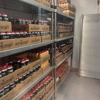 Great Notion - Berkeley - Metal shelving units in a storage room are stocked with rows of canned beer, with some boxes labeled #KEEPBEERFUN. The shelves are organized with cans stacked neatly, and the room has a plain white wall and a gray floor. A metallic panel or door is partially visible on the right side of the image. - Brewpubs Near Me - Berkeley, California