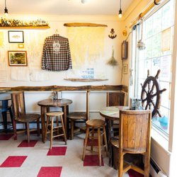 Panacea - The window seats at Panacea. Upcycled boat tables, a wooden ship steering wheel, upcycled shirts and art in the background.