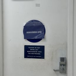 A plain white door features two signs: one says 'associates only,' and another requests no merchandise in restrooms. A keypad lock is installed on the door.