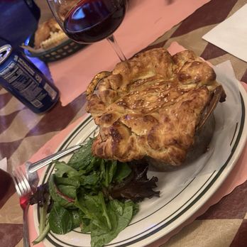 Depot - Chicken pot pie - A chicken pot pie with a golden, flaky crust is served on a plate with a side salad of mixed greens, alongside a glass of red wine. - Bars Near Me - Caledonia, Wisconsin