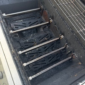 Grill Guard - BEFORE - The photo depicts the interior of a barbecue grill with multiple metal grates and components removed, revealing the empty cooking chamber. The remaining parts include some metal supports and a wire rack at the top. The interior surfaces show signs of use, with soot and residue present. The image focuses on the empty, cleaned or disassembled state of the grill, highlighting its internal structure. - Grill Services Near Me