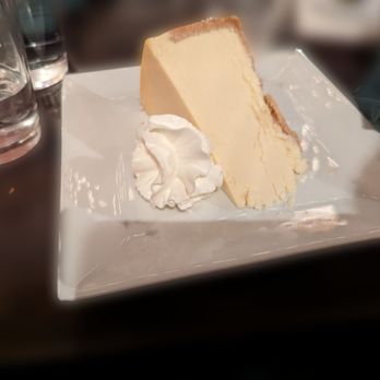 PC's Paddock Restaurant - 12/21/23 - Cheesecake with whipped cream, tasty and the way to close the night. - A slice of cheesecake with a dollop of whipped cream on a white square plate, placed on a dark table. - American Near Me - Poughkeepsie, New York