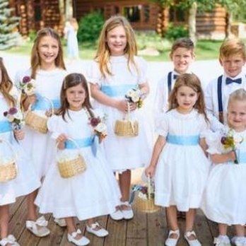 Scarlet Oak Studio - Children in white dresses and shirts, holding baskets and flowers, standing outdoors on a wooden deck during a celebration. - Videographers Near Me - Provo, Utah