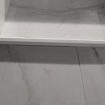 Modern Concepts - Missing grout/waterproofing in shower - A photo showing a shower ledge with visible gaps where grout or waterproofing is missing, with marble-like tiles. - General Contractors Near Me