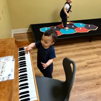 Bumblebee Playspace - Having fun in the music room! - Children are engaged in activities in an indoor play area, with one child playing the piano and another on a game platform in the background. - Indoor Playcenter Near Me - Newark, California