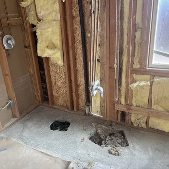 Carpeteria - A room under renovation with exposed wall studs, yellow insulation, visible plumbing pipes, and a hole in the concrete floor. - Carpeting Near Me - Lancaster, California