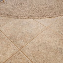 After - The image shows beige ceramic tiles with grout lines and a textured, light brown rug at the top edge.