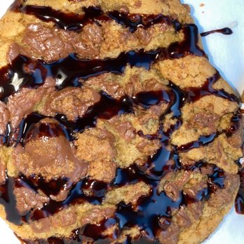 The Cookie Connect - Stuffed Peanut Butter Cup Cookie - A large cookie with chocolate chunks, drizzled with chocolate syrup, and colorful sprinkles visible at the top edge. - Desserts Near Me - Bloomfield, New Jersey