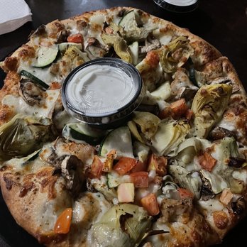 Maxwells Eatery - My small(9"/$14) Garlic Chicken pizza w/zucchini, mushrooms, artichokes, tomatoes & Ranch was AWESOMENESS! - A pizza featuring toppings such as zucchini, artichokes, mushrooms, and cheese, with a golden-brown crust. A small container of ranch dressing is placed on top of the pizza. The pizza is on a dark table, with a glass of water and another pizza partially visible in the background. - Pizza Near Me - Redding, California