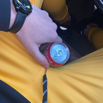 Exxon - a person holding a can of soda - A person in yellow pants is holding a soda can with a black and white lanyard attached, wearing a black watch, inside a vehicle. - Car Wash Near Me - Spring, Texas
