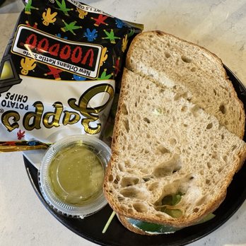Hexe Coffee - Garden Me - Three slices of bread, a small container of olive oil, and a bag of New Orleans-style potato chips are on a black plate. - Coffee & Tea Near Me - Chicago, Illinois