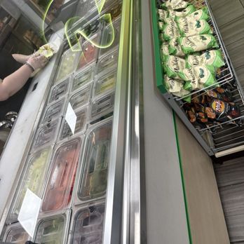 Subway - clean presentation - A worker wearing gloves is preparing food behind a glass display case at a Subway restaurant, with shelves of packaged snacks nearby. - Sandwiches Near Me - Willows, California
